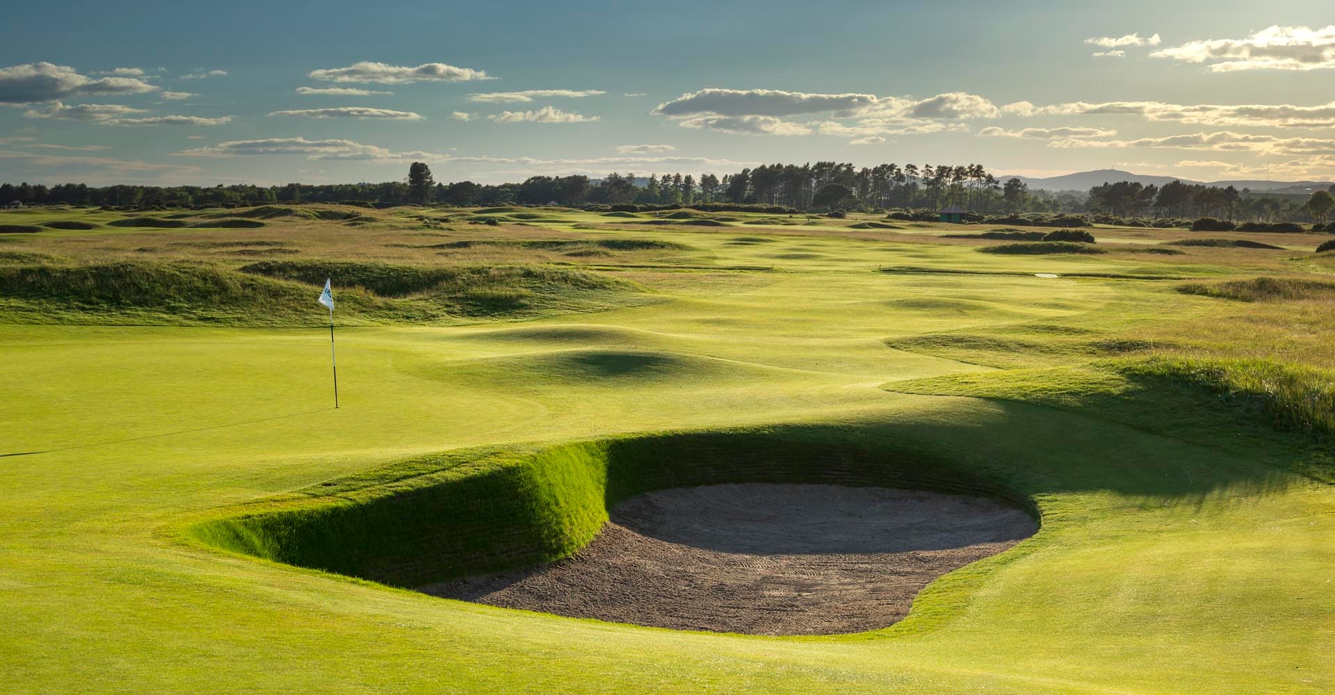 A well maintained fairway leading to a smooth green next to a sand bunker in Scotland