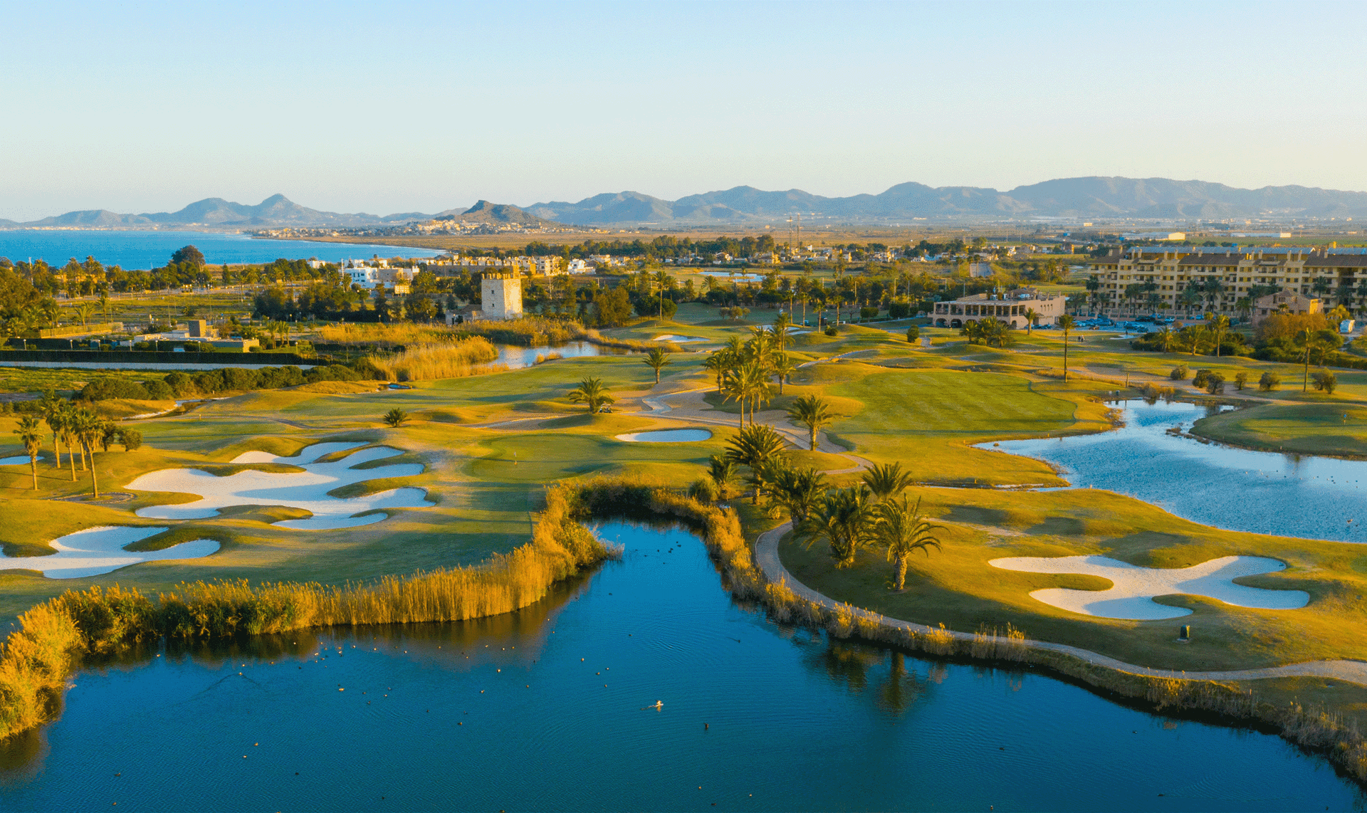 A well maintained fairway nestled with sand bunkers next to a water hazard