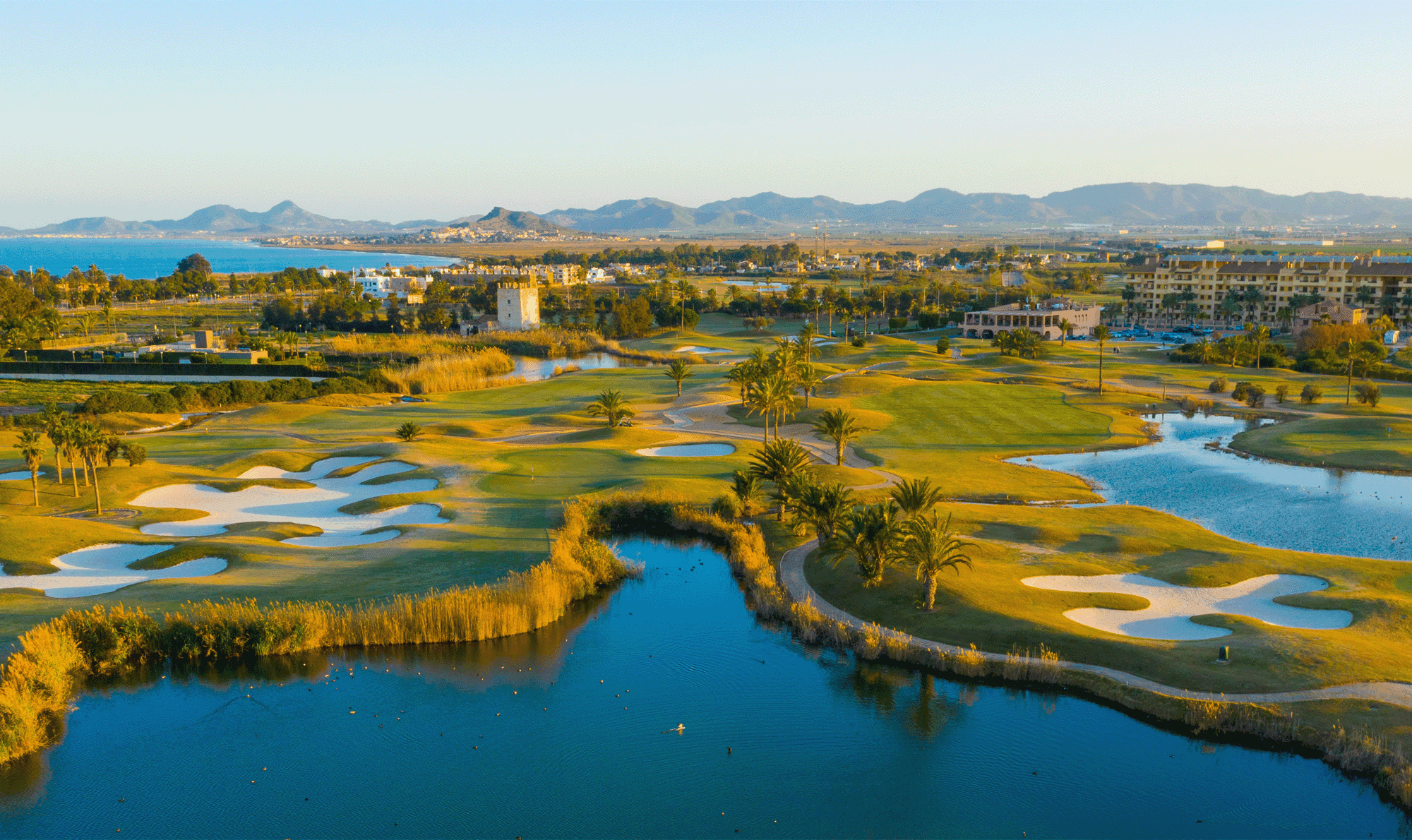 A well maintained fairway nestled with sand bunkers next to a water hazard