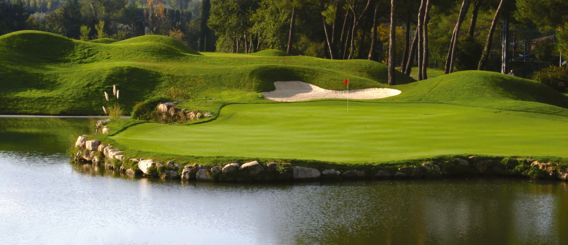 A smooth green with a red flag stick next to a large sand bunker