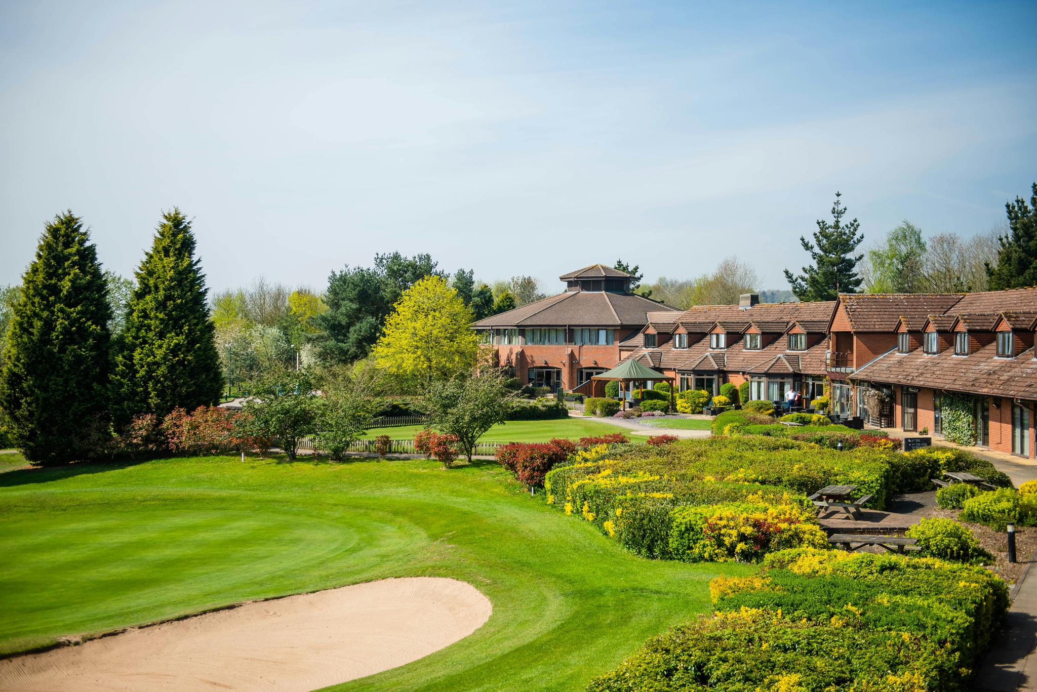 Panoramic view of the clubhouse overlooking a smooth green next to a large sand bunker