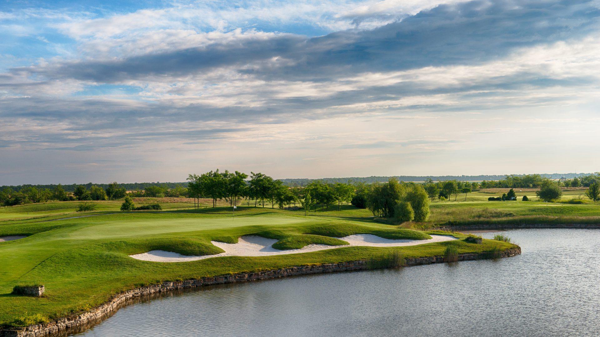 A well maintained fairway with sand bunkers next to a water hazard