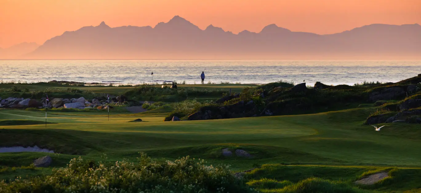 A well maintained fairway with the sun setting behind distant mountain views