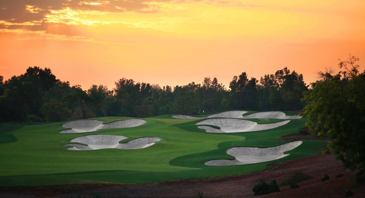 A smooth green surrounded by sand bunkers at sunset