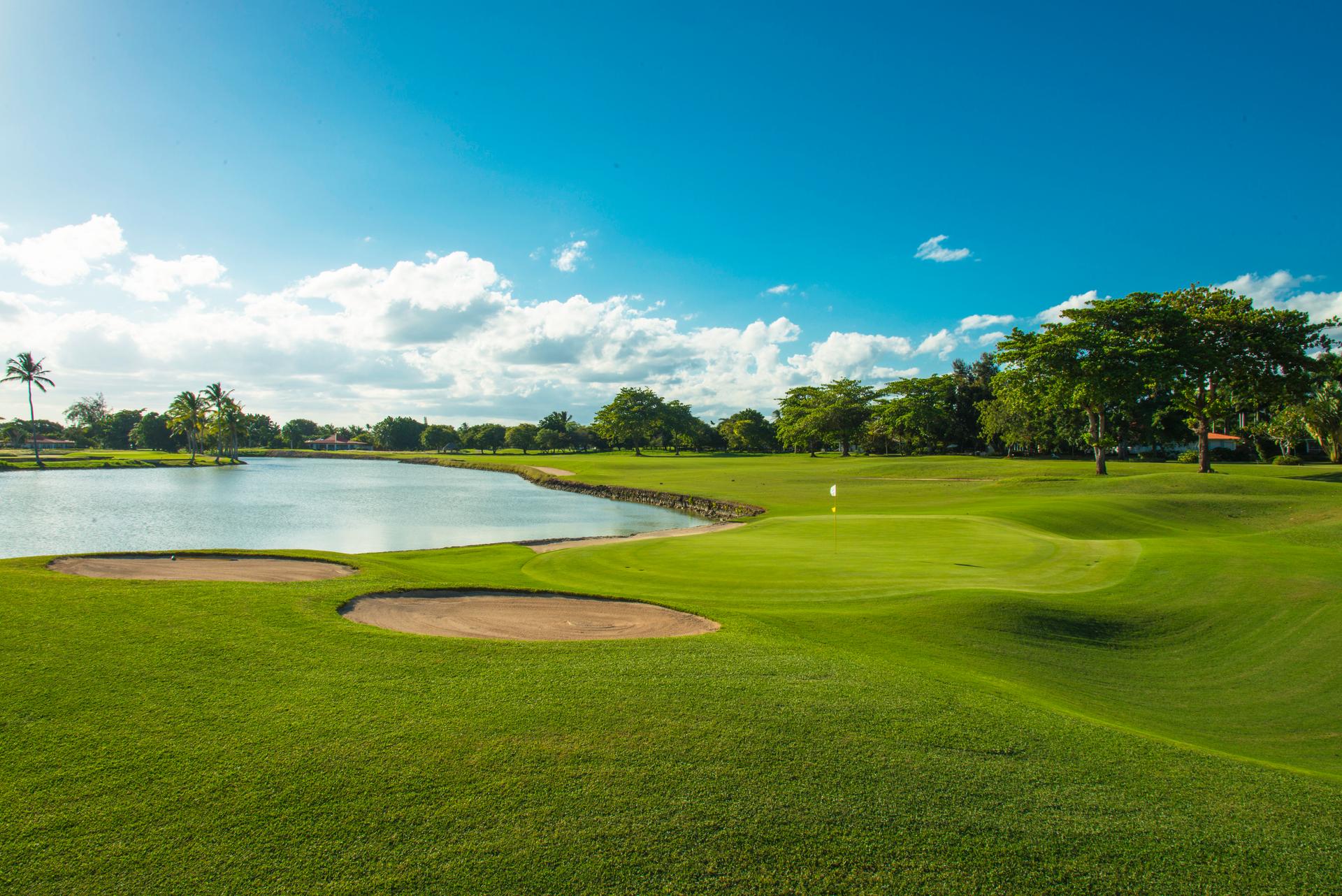 A well maintained green next to a sand bunker and water hazard