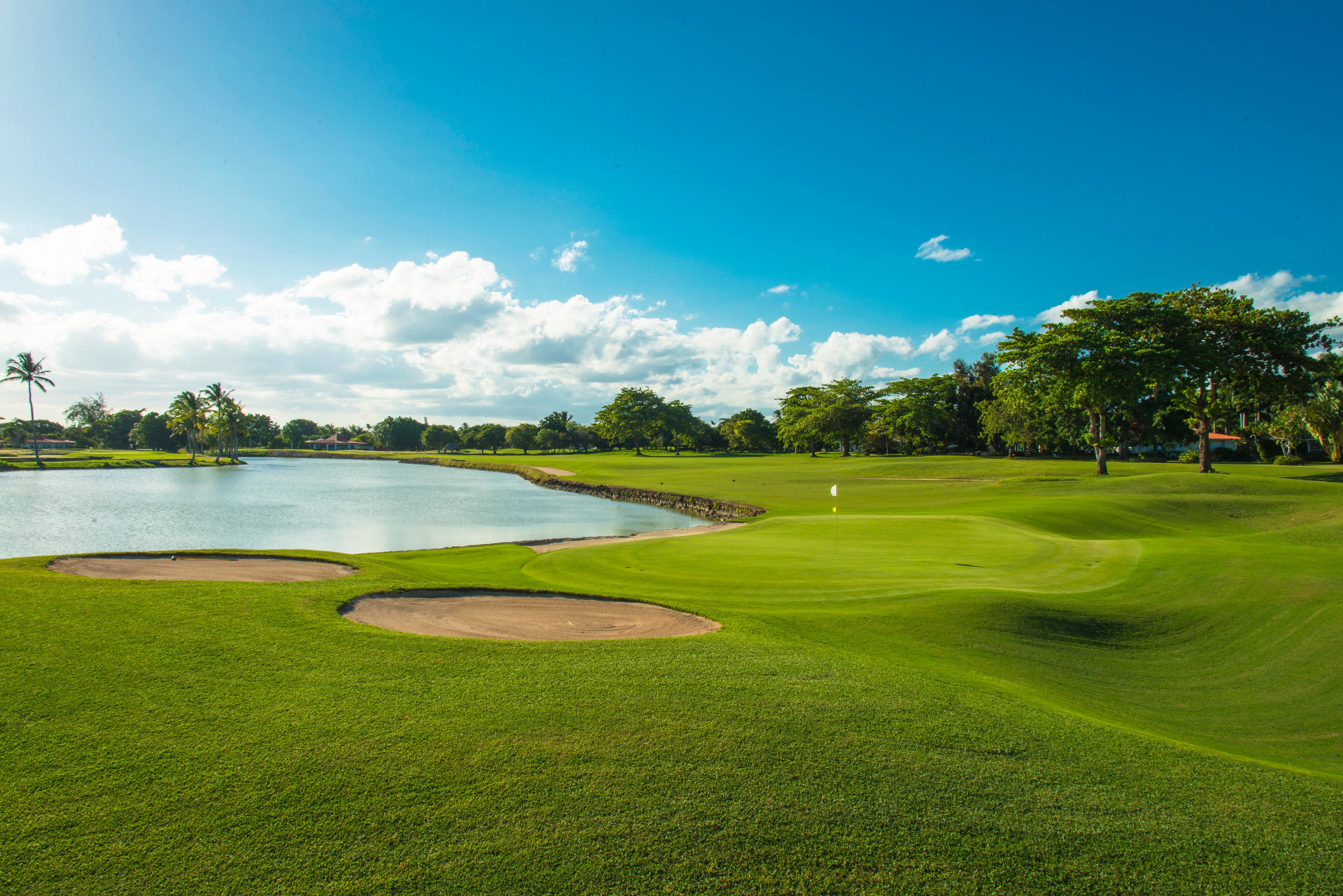 A well maintained green next to a sand bunker and water hazard