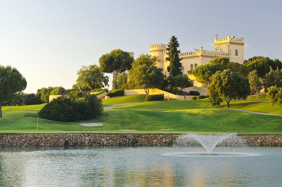 Water hazard (foreground) in front of a green with the castle-faced clubhouse in the background