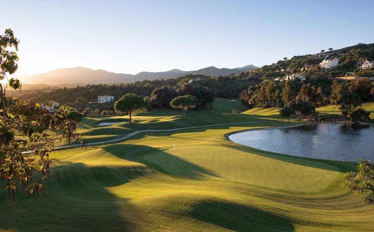 A smooth green surrounded by rolling dunes next to a water hazard