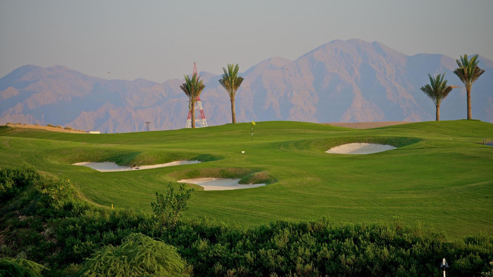 A well maintained fairway nestled with sand bunkers with distant mountain views