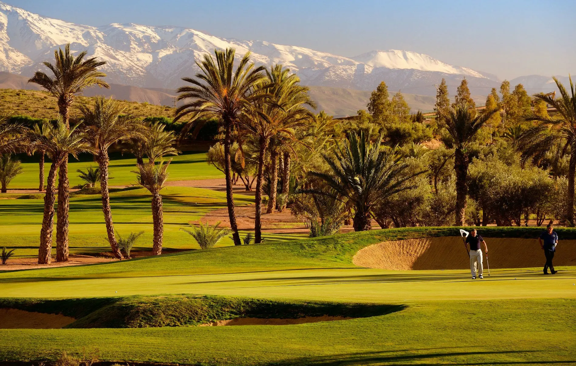 A well maintained fairway nestled with a sand bunker and mountain views in the distance