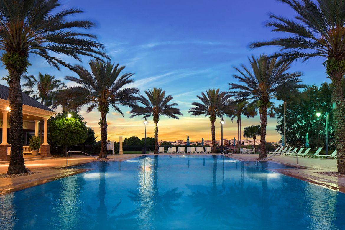 Outdoor swimming pool surrounded by palm trees with the sun setting in the distance