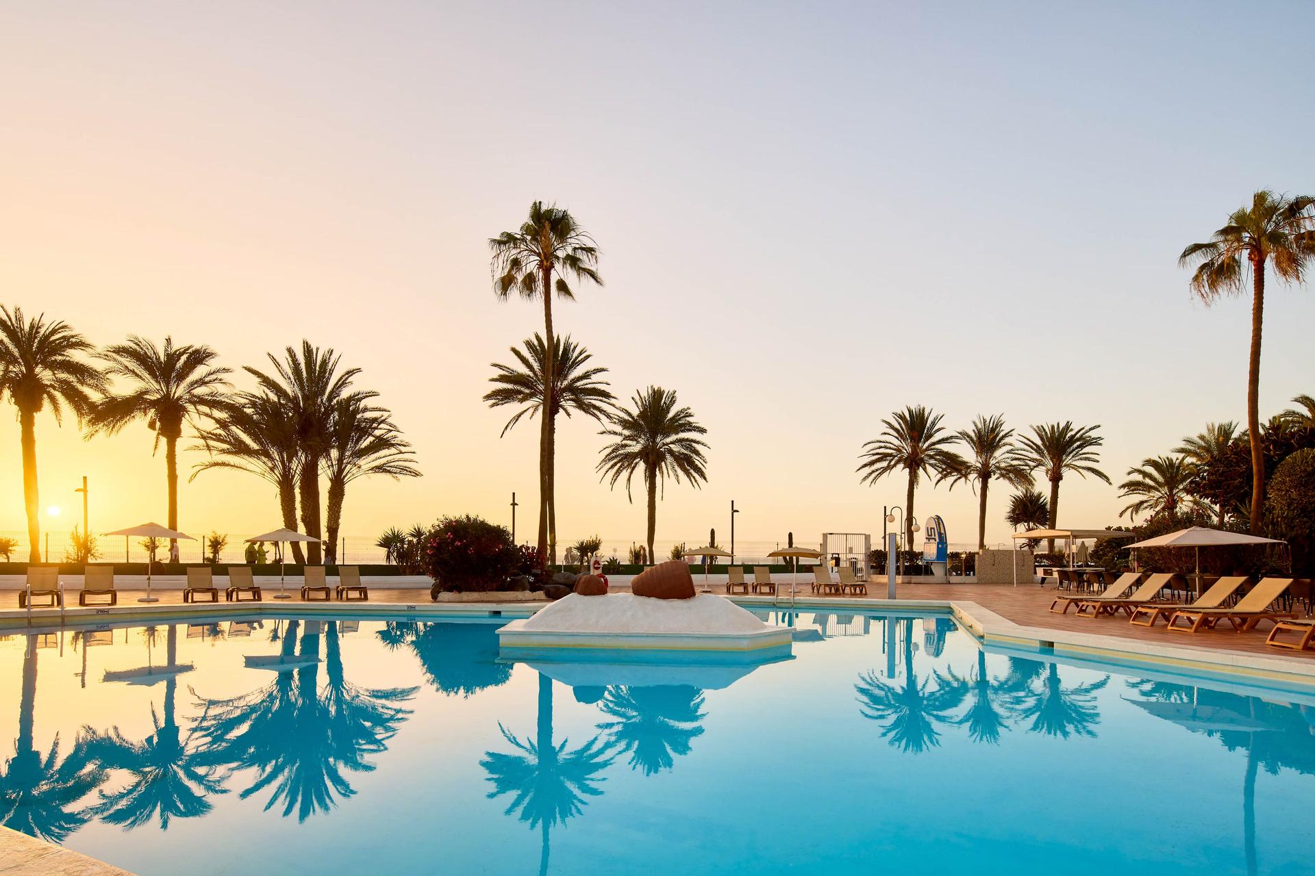 Sun setting in the distance over the outdoor swimming pool at Sol Tenerife Hotel