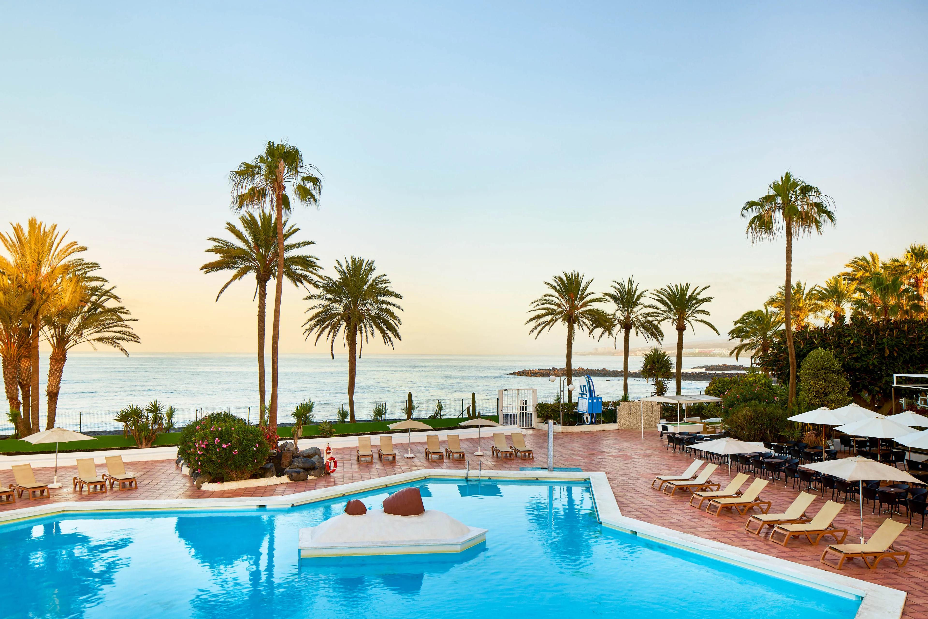 Outdoor swimming pool lined with palm trees at Sol Tenerife Hotel