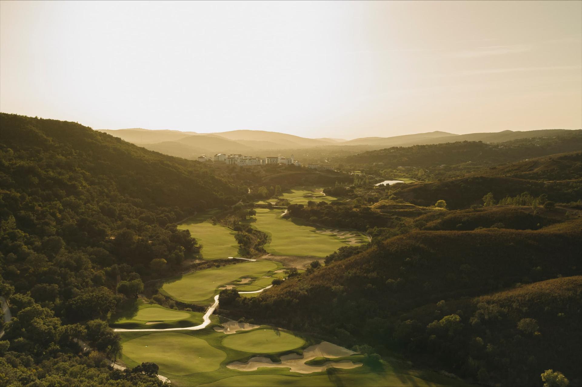 A well maintained fairway with sand bunkers with the sun shining on the course