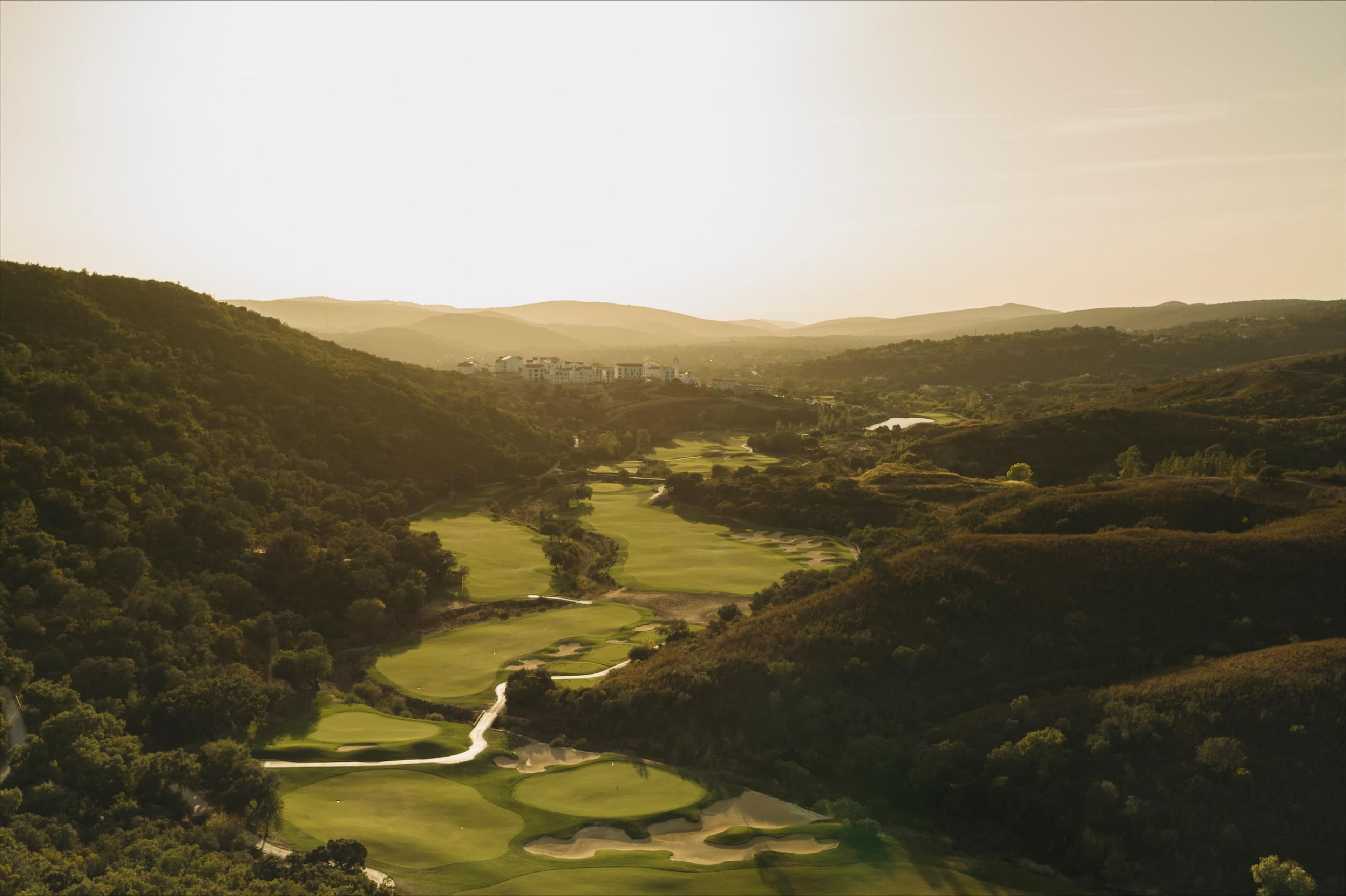 A well maintained fairway with sand bunkers with the sun shining on the course