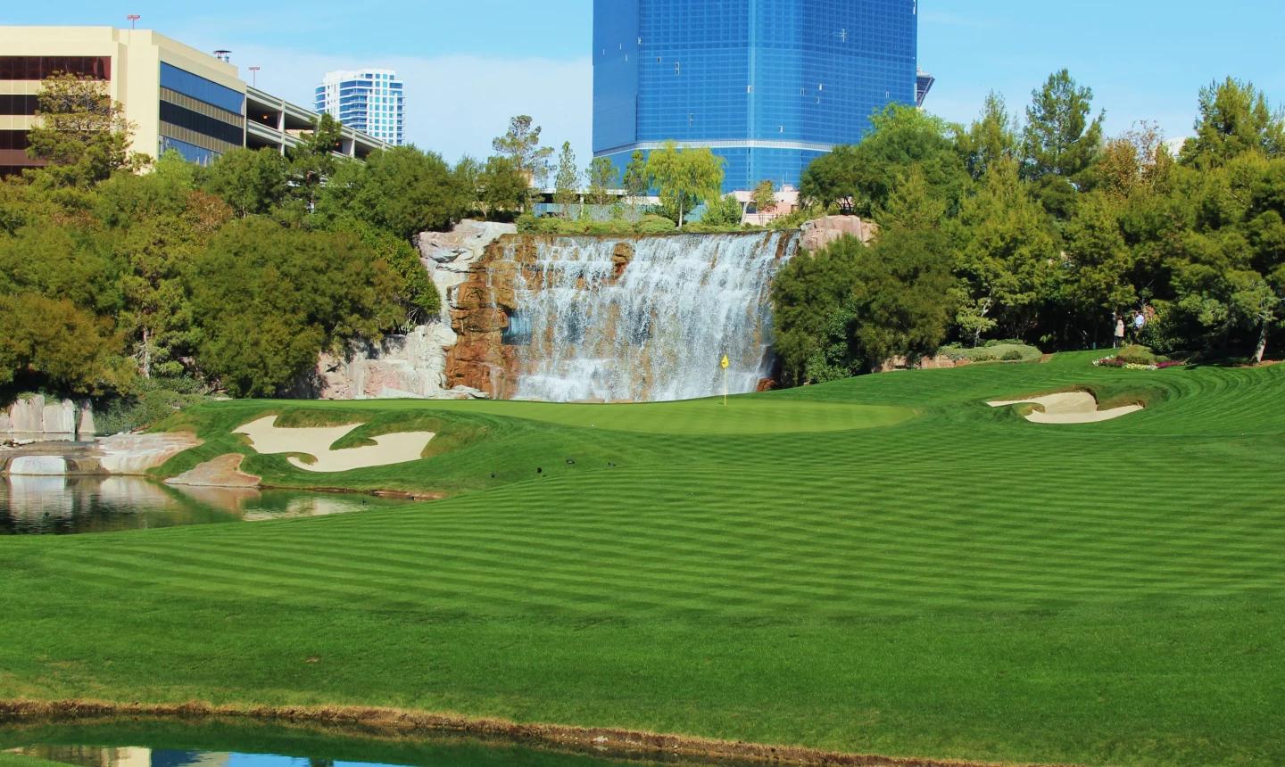 A well maintained fairway leading to a smooth green with a water fountain in the background