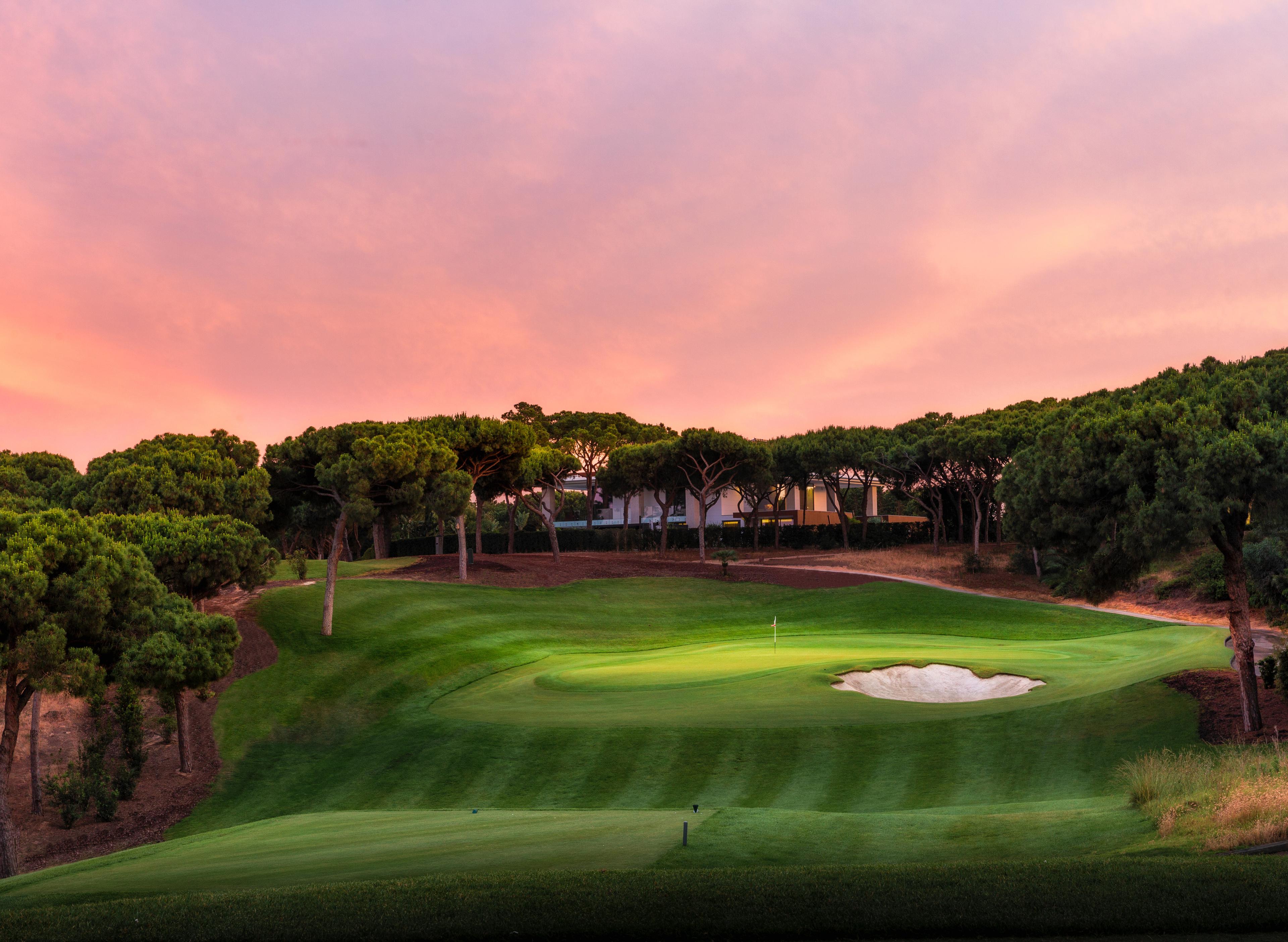 A well maintained fairway leading to a smooth green under the sunset