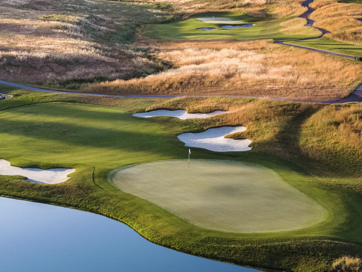 Panoramic view of a manicured green surrounded by sand bunkers next to a water hazard