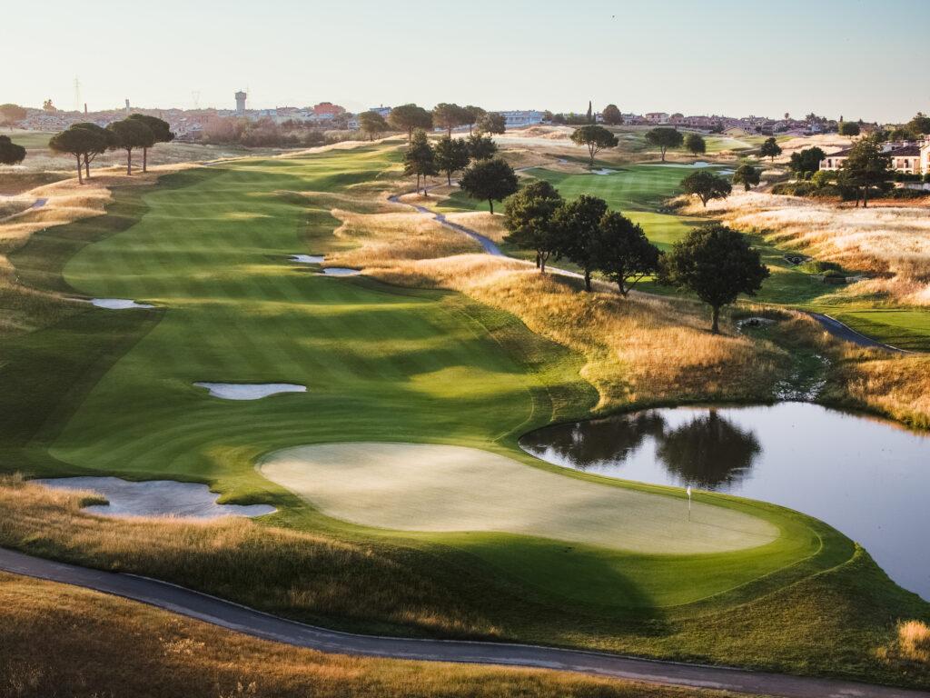 Overhead view of a well maintained fairway nestled with sand bunkers leading to a smooth green next to a water hazard