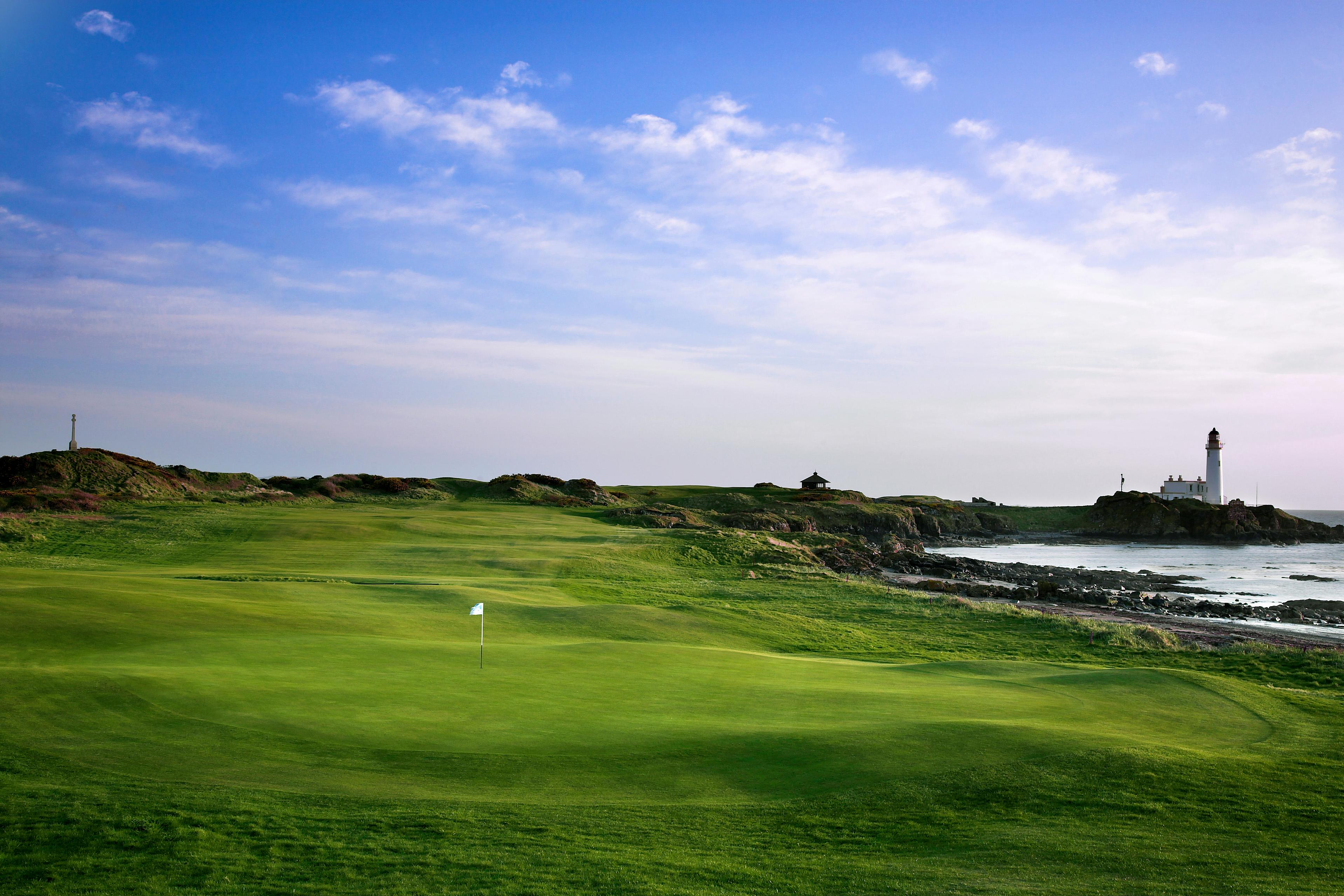 A well maintained fairway leading to a smooth green with a lighthouse in the distance
