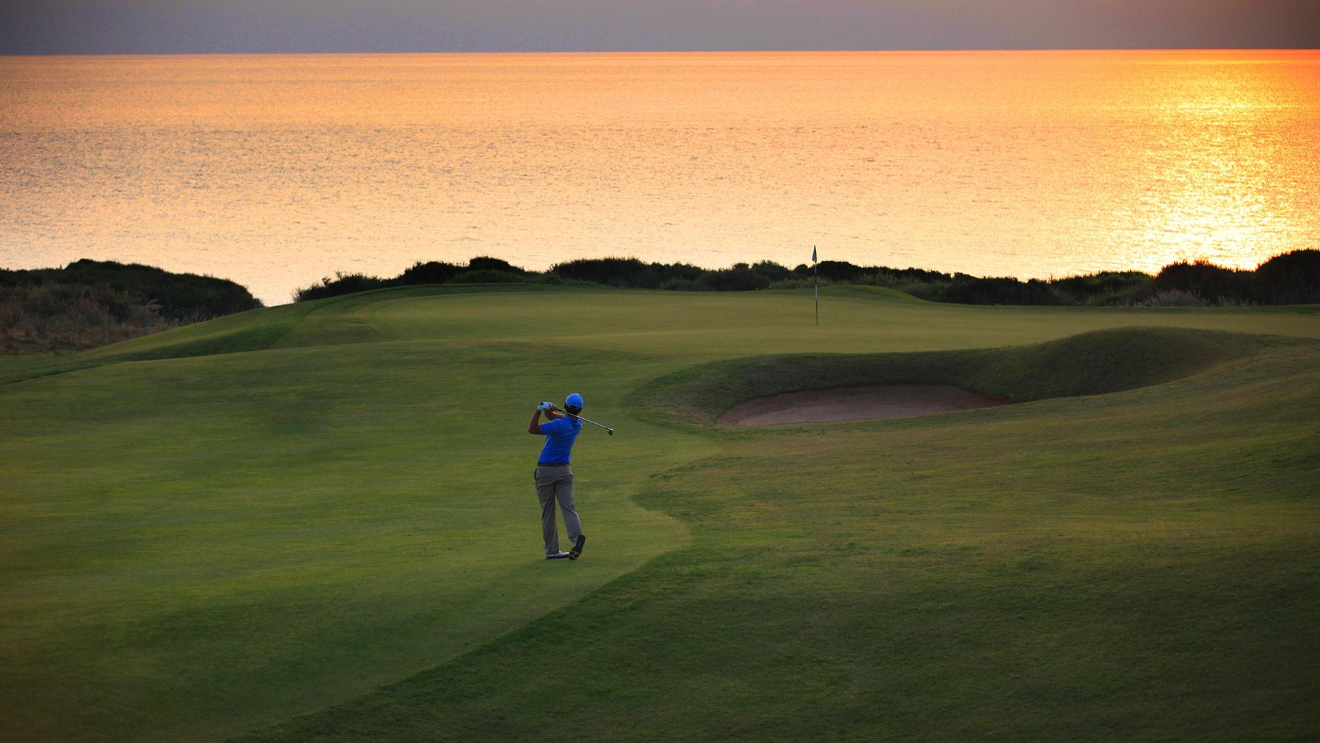 A golfer swinging on a manicured fairway under the sunset