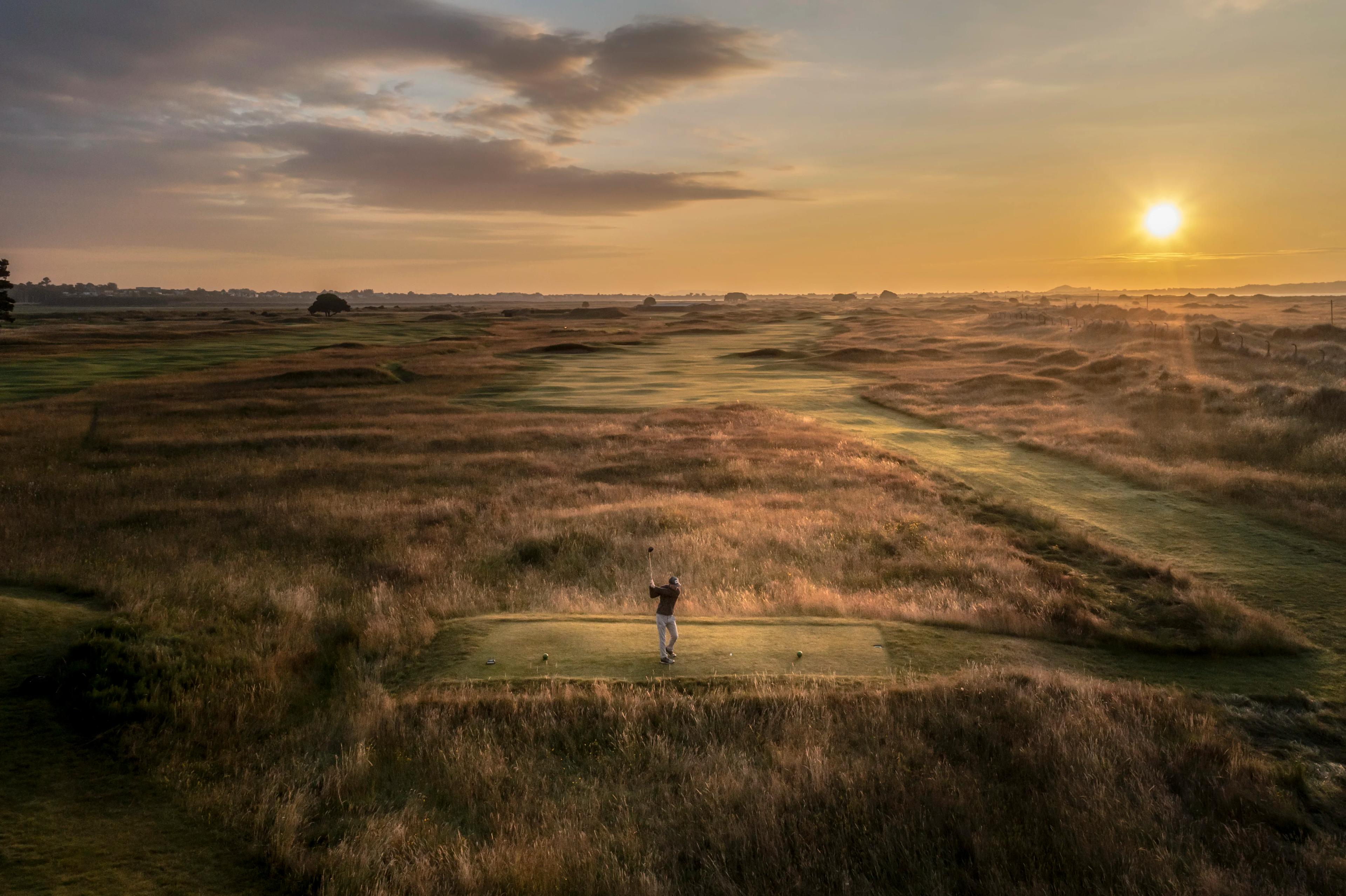 golfer swinging at sunset on a pitch with tall grass