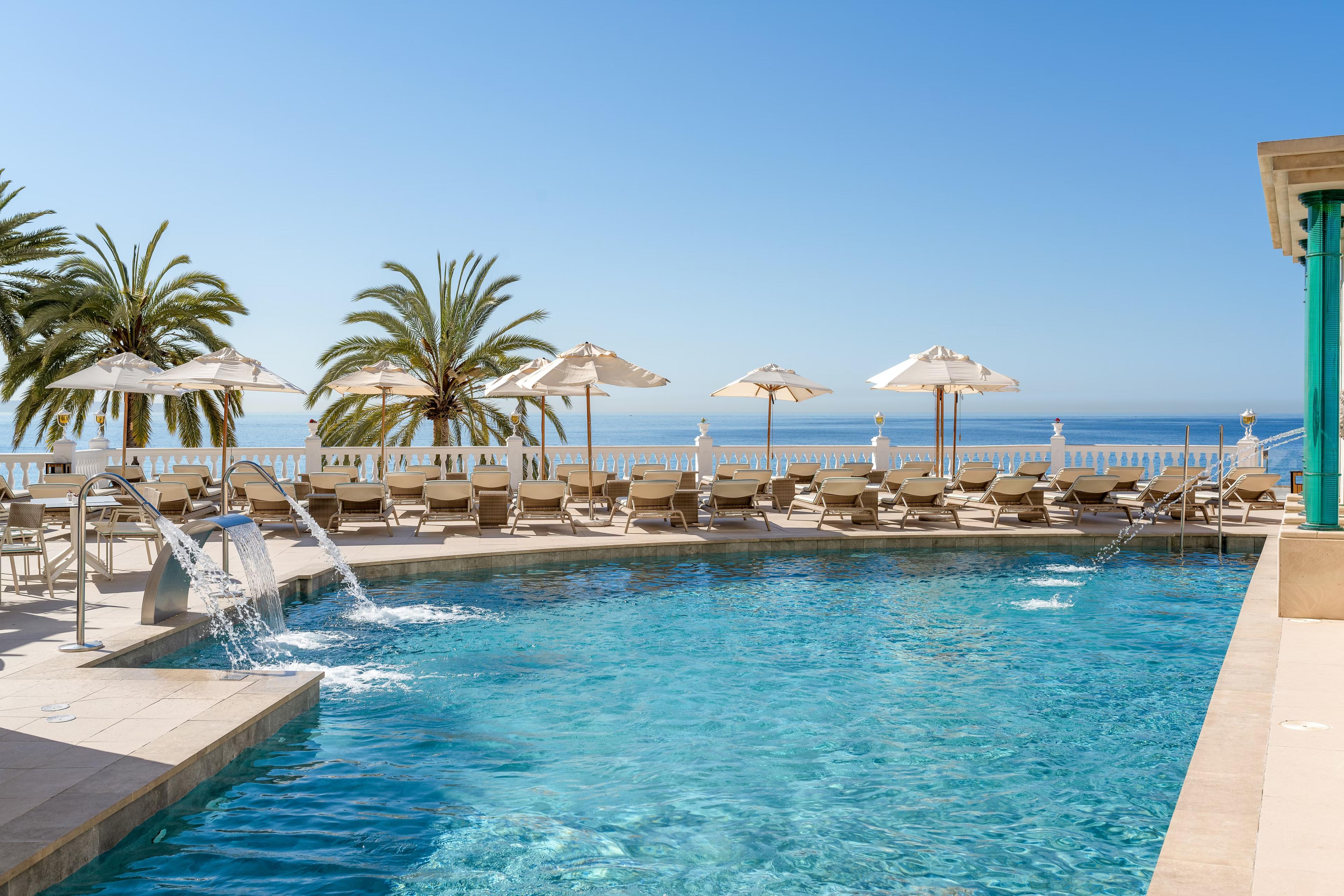 Outdoor pool lined with sunbeds under clear blue skies