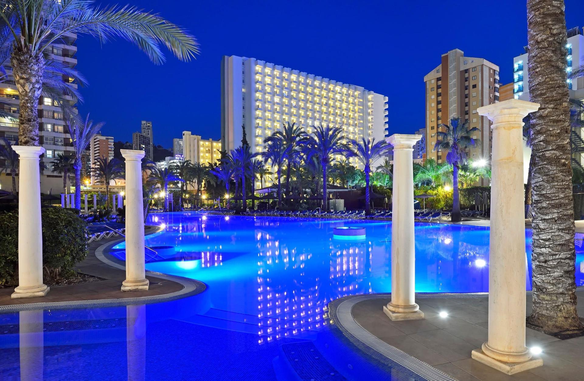 Panoramic view of the Hotel Sol Pelicanos Ocas building overlooking the pool lit up at night time