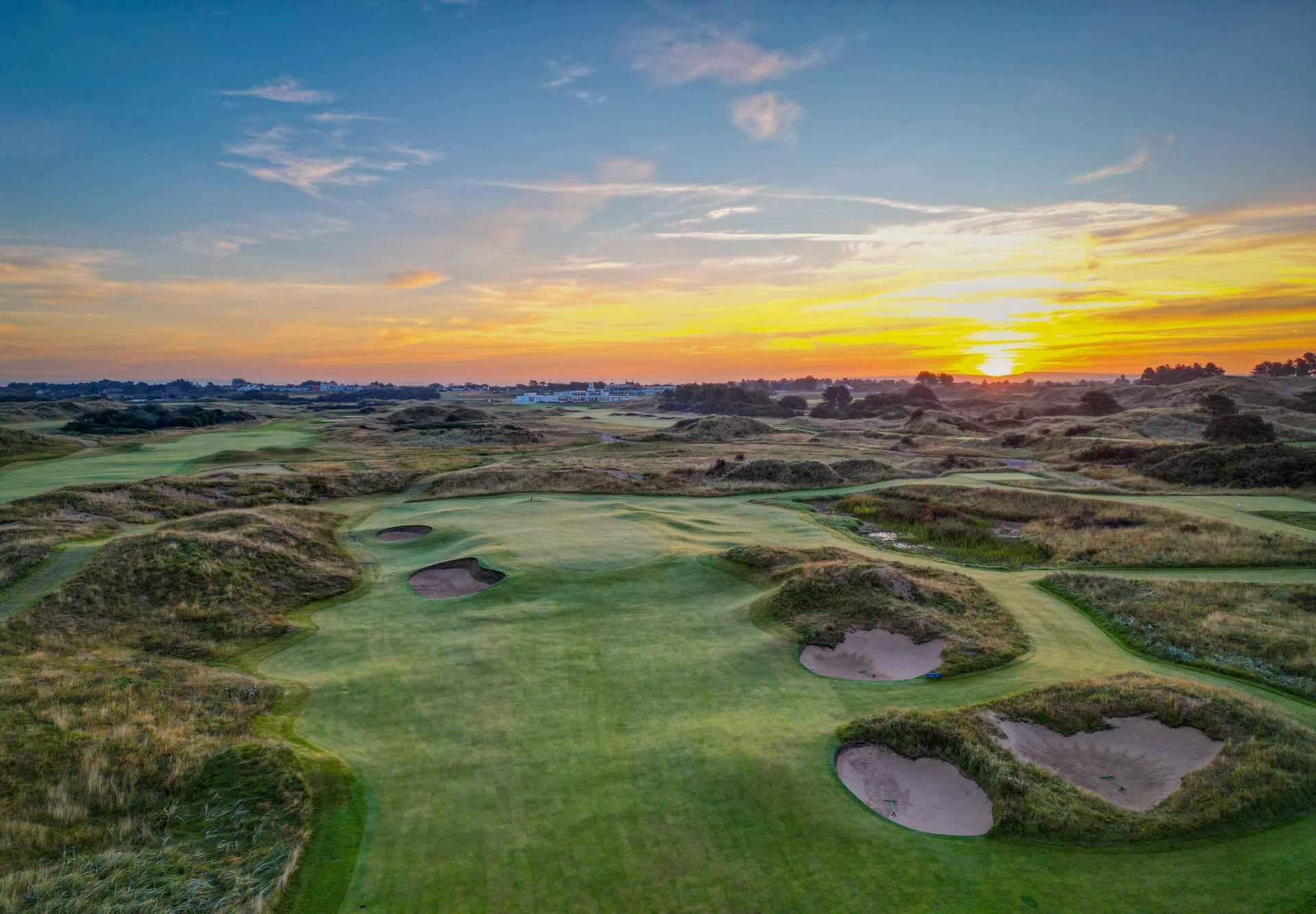 A well maintained fairway nestled with sand bunkers under the sunset