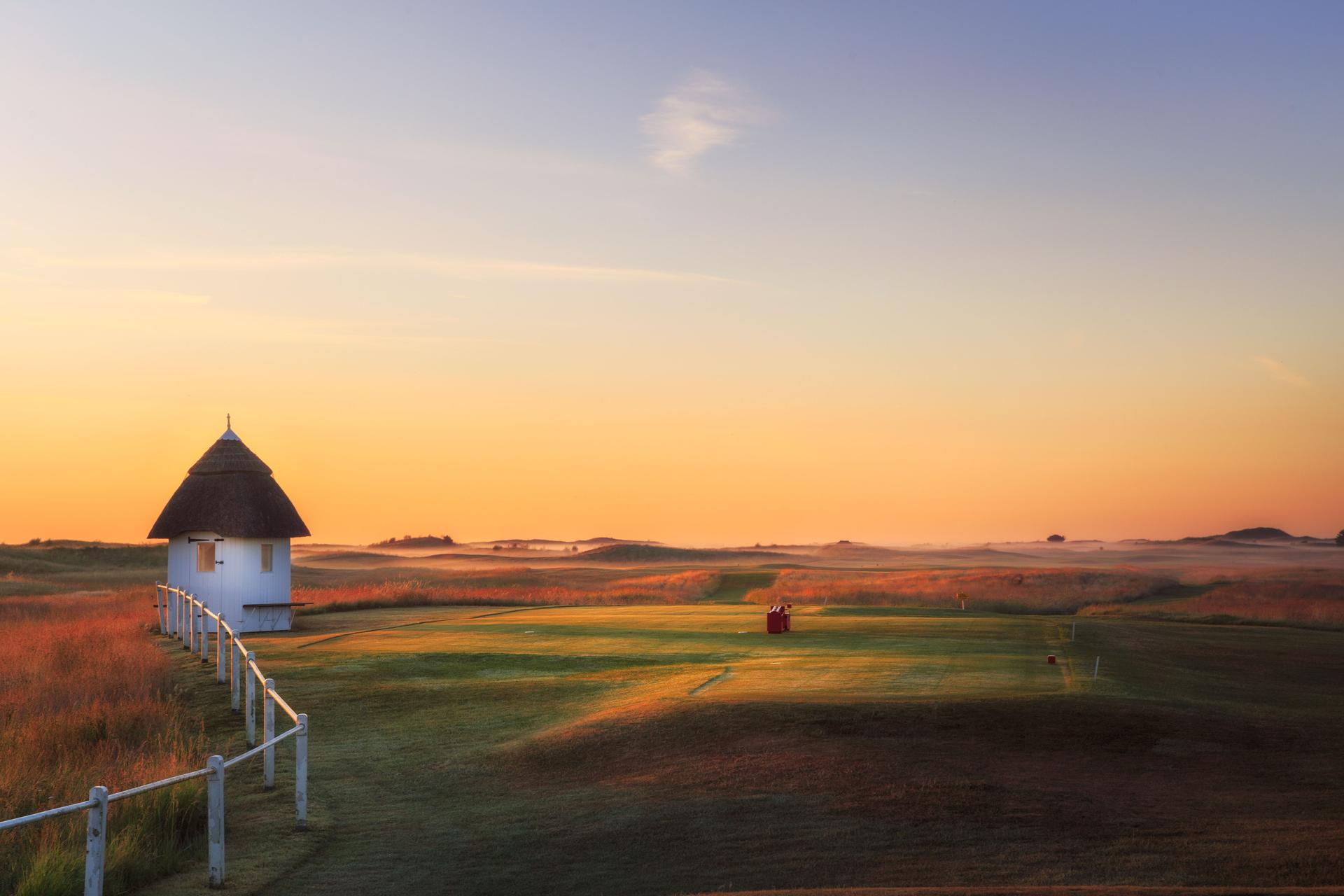 A well maintained fairway with a sunset in the distance