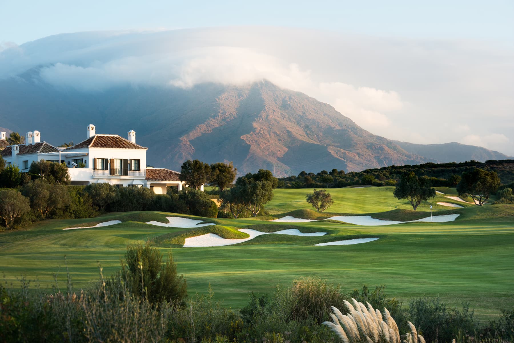 A well maintained fairway nestled with sand bunkers and mountain views in the distance