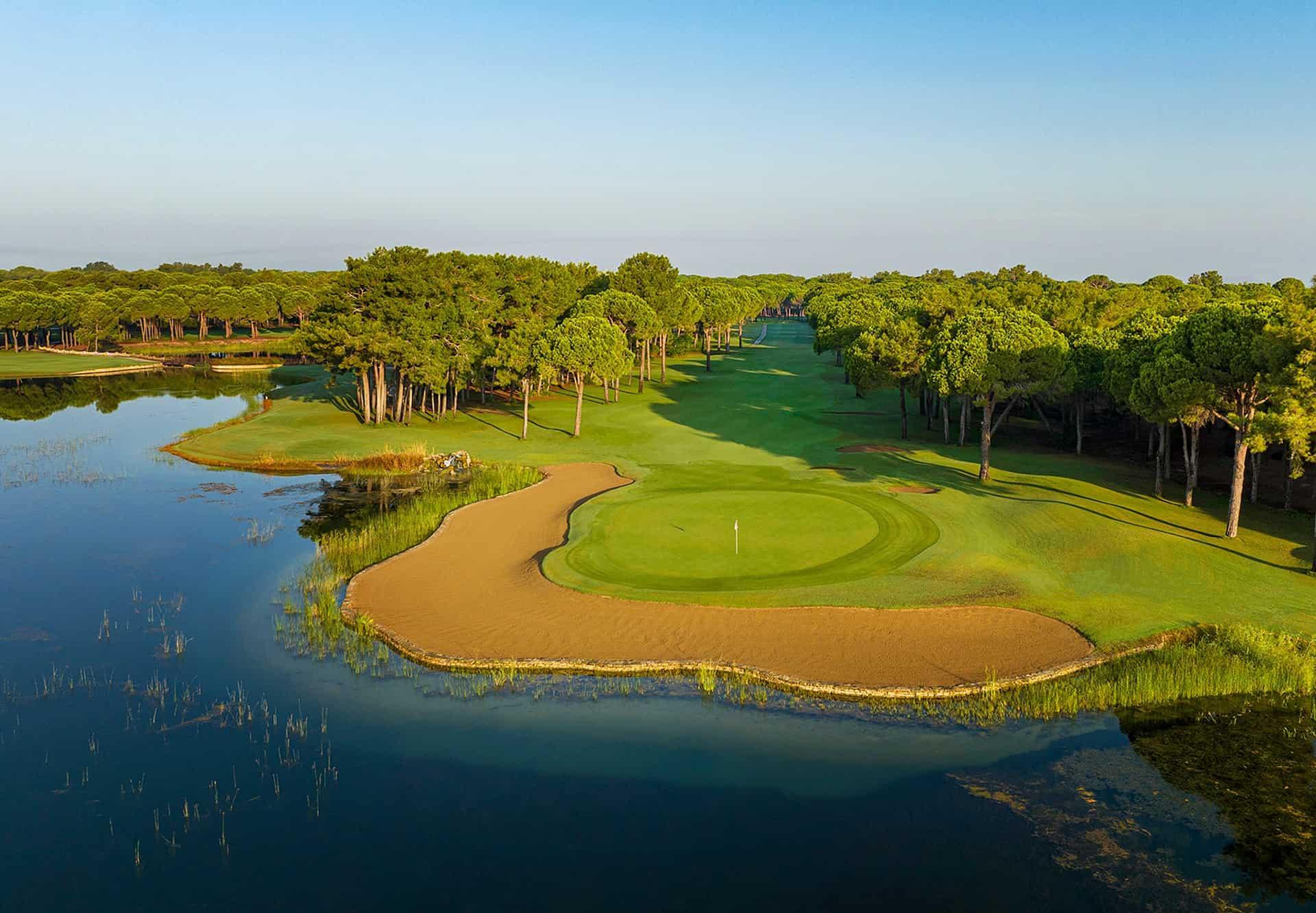 Aerial view of a tree-lined fairway leading to a green with a large water hazard behind it (foreground)