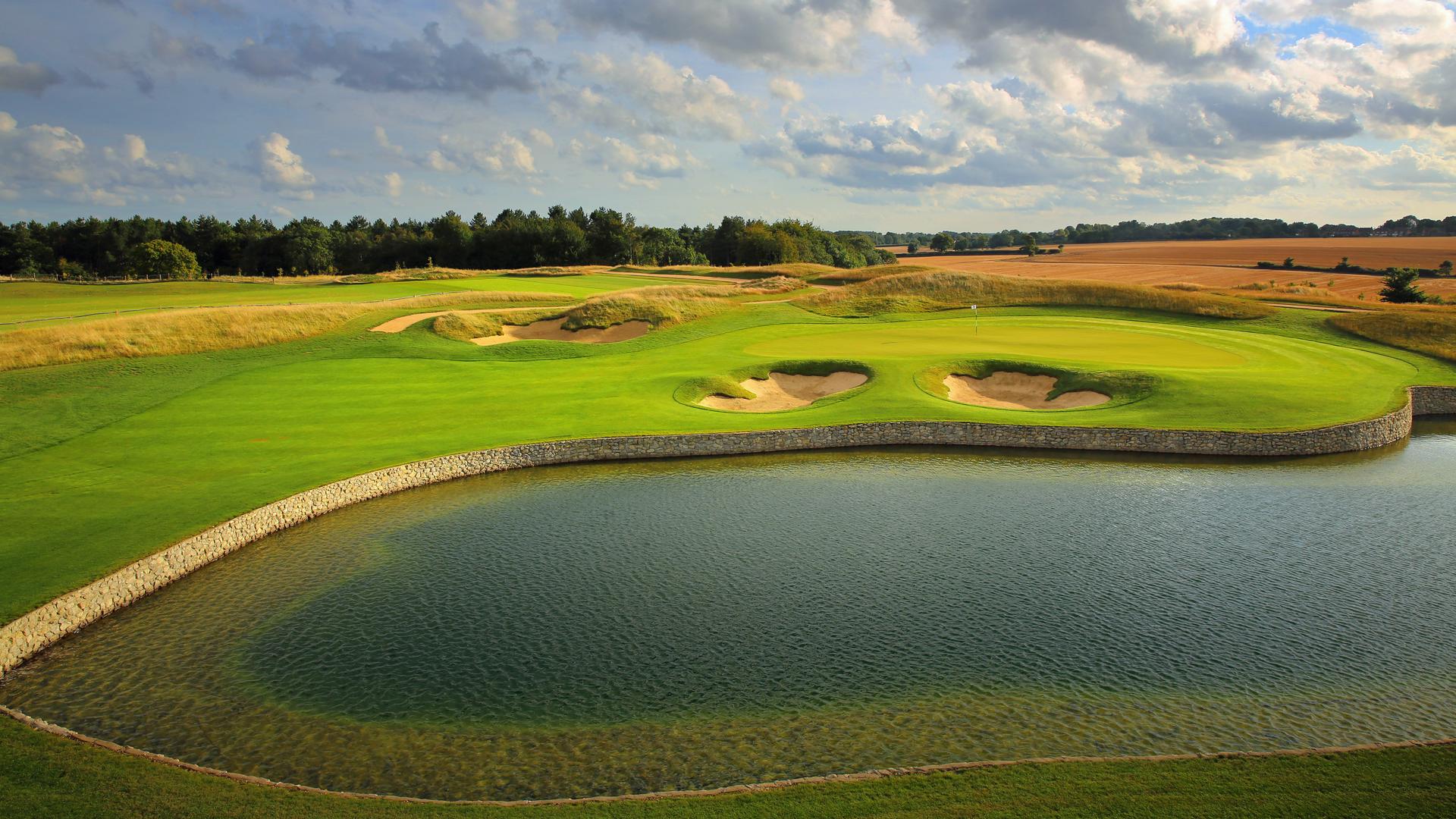 A well maintained fairway next to a water hazard nestled with sand bunkers