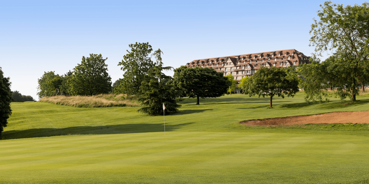 Panoramic view of a well maintained fairway with the Hotel Barriere L'Hotel du Golf in the background