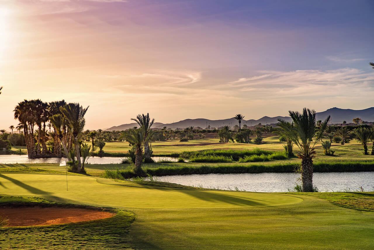 A smooth green next to a sand bunker under the sun