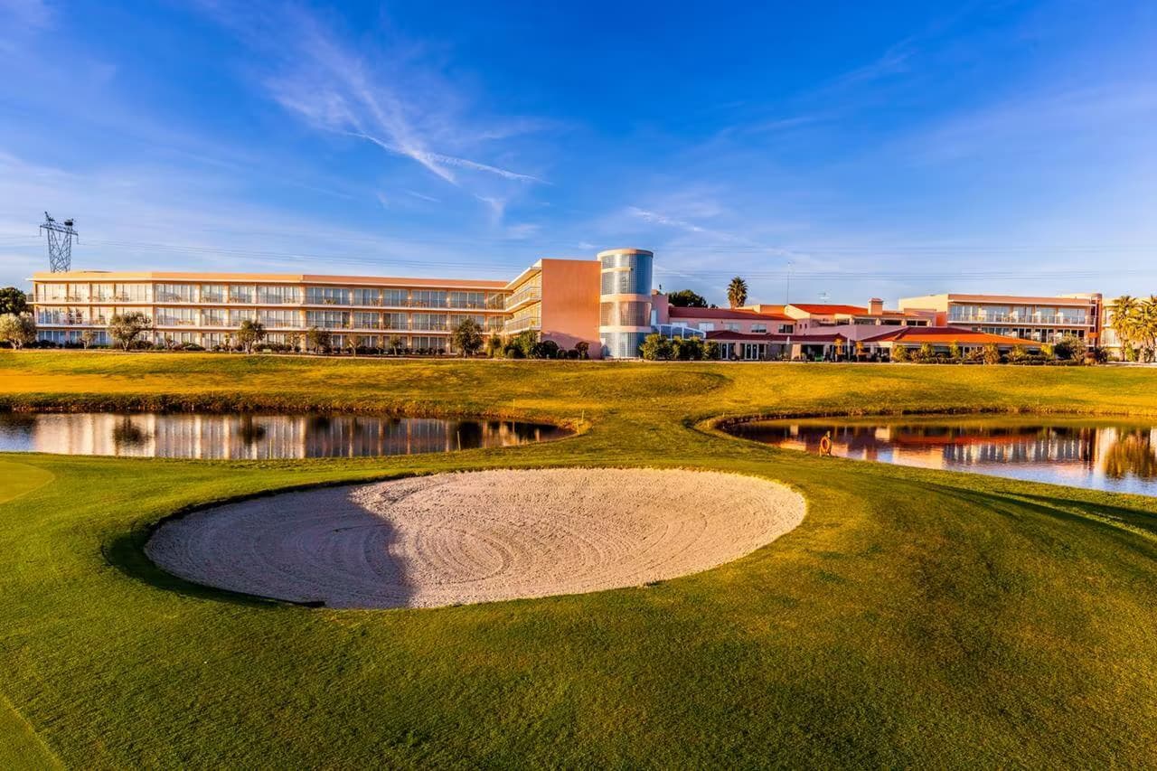 A well maintained fairway with a sand bunker and the Montado Hotel & Golf Resort building in the back