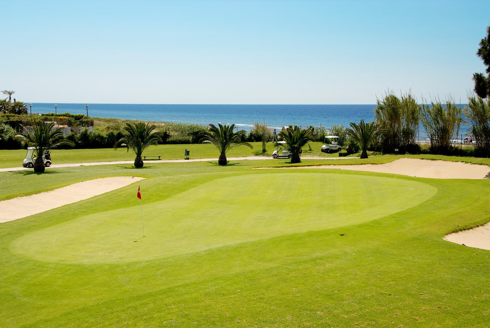A smooth green surrounded by sand bunkers with coastal views