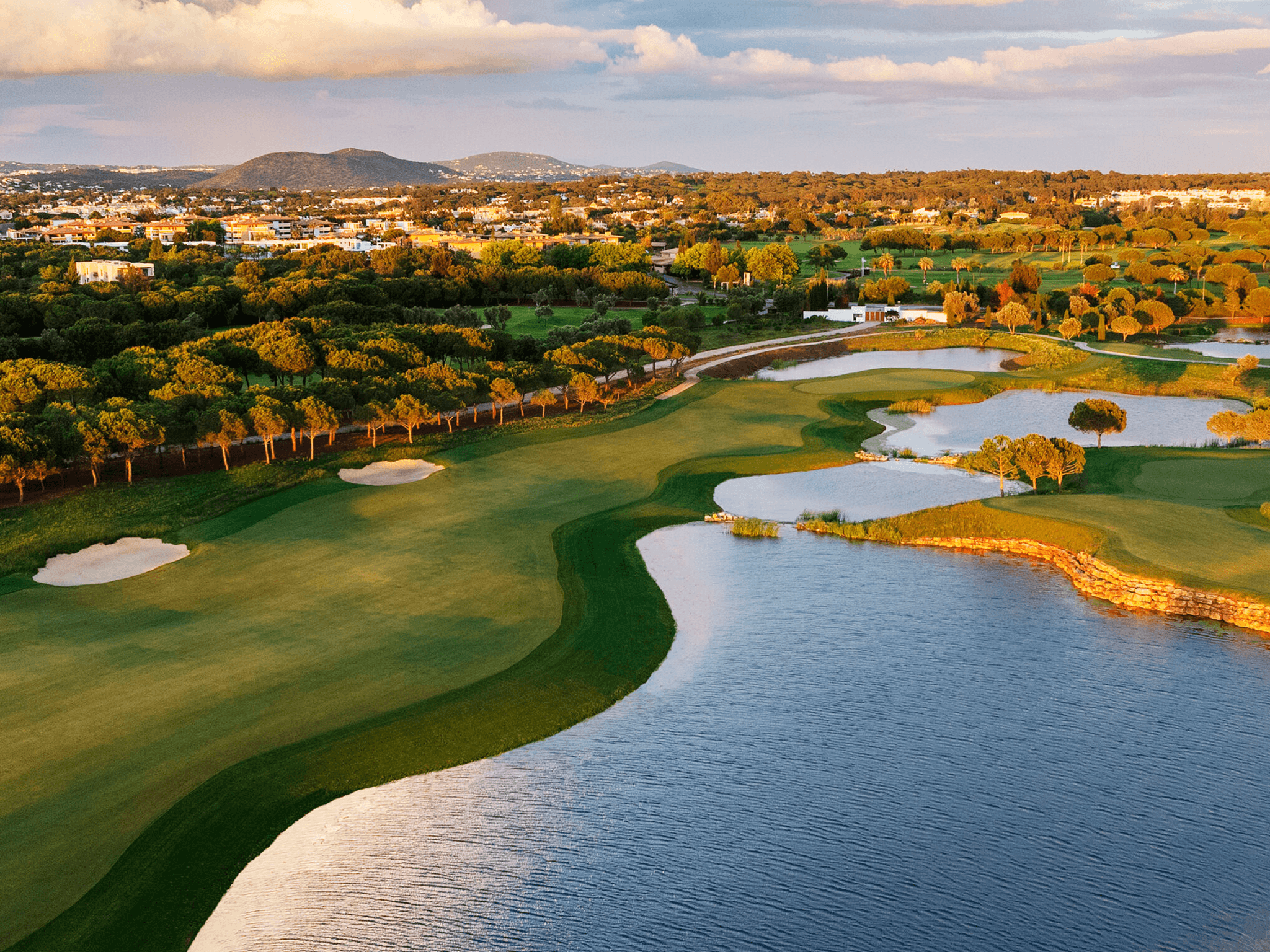 A well maintained fairway nestled with sand bunkers next to a water hazard