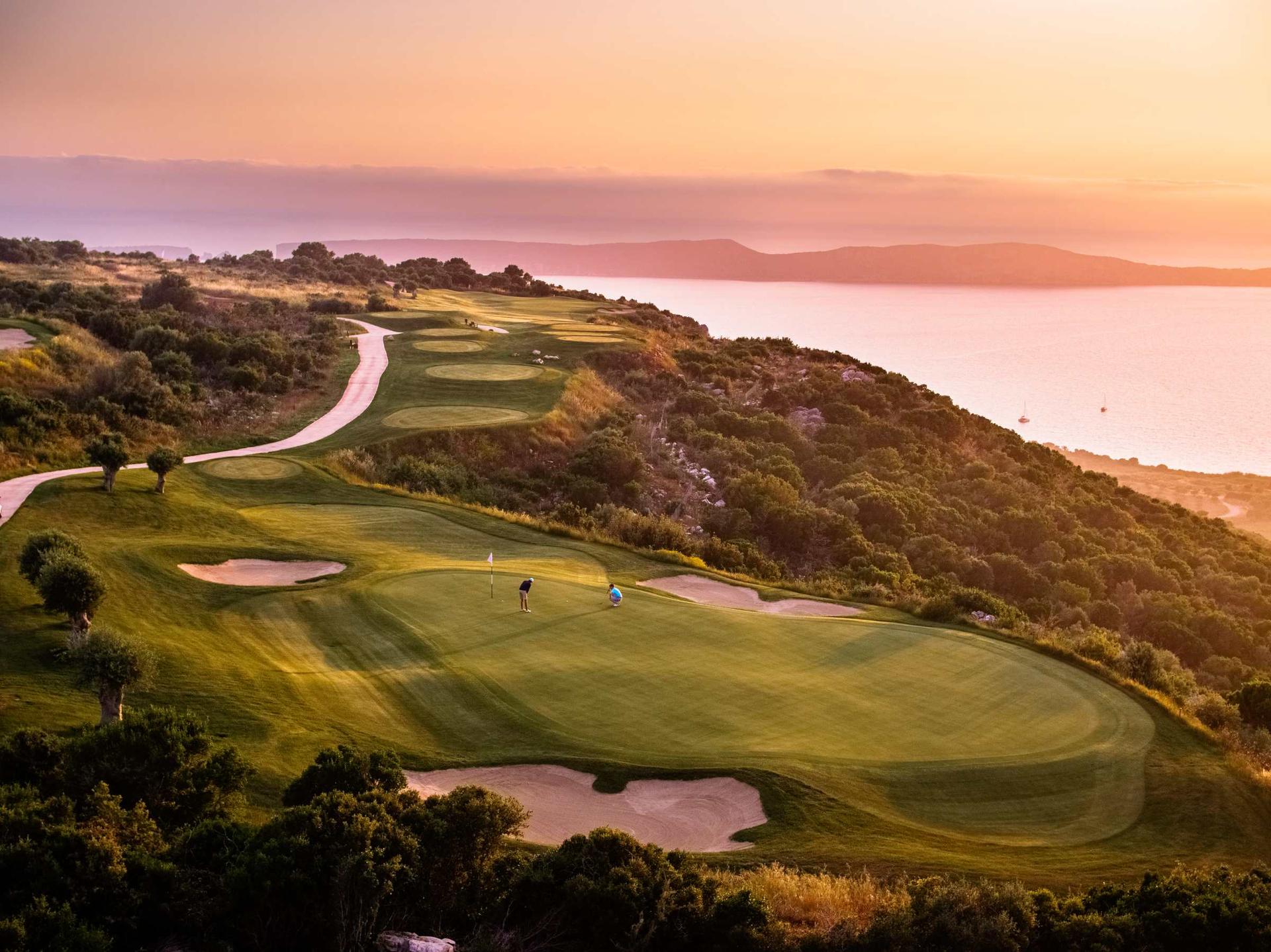 A smooth green surrounded by sand bunkers under the sunset