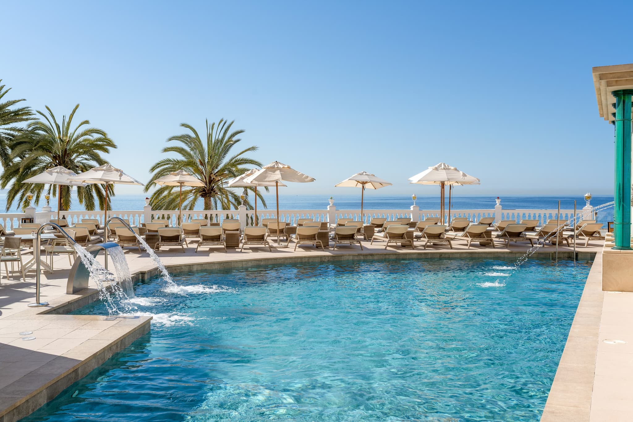 Outdoor pool lined with sunbeds under clear blue skies
