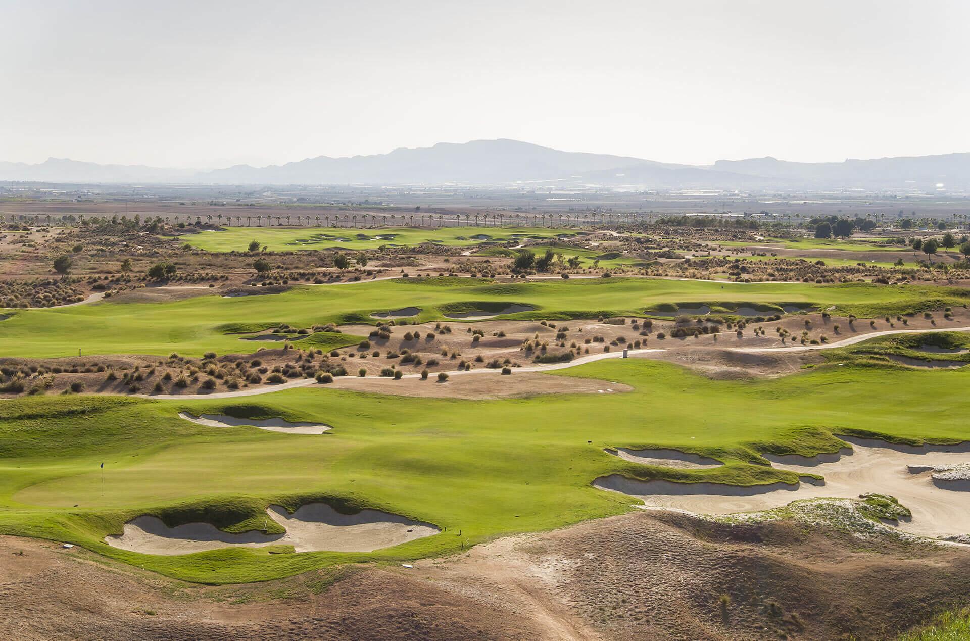 A well maintained fairway nestled with sand bunkers with distant mountain views