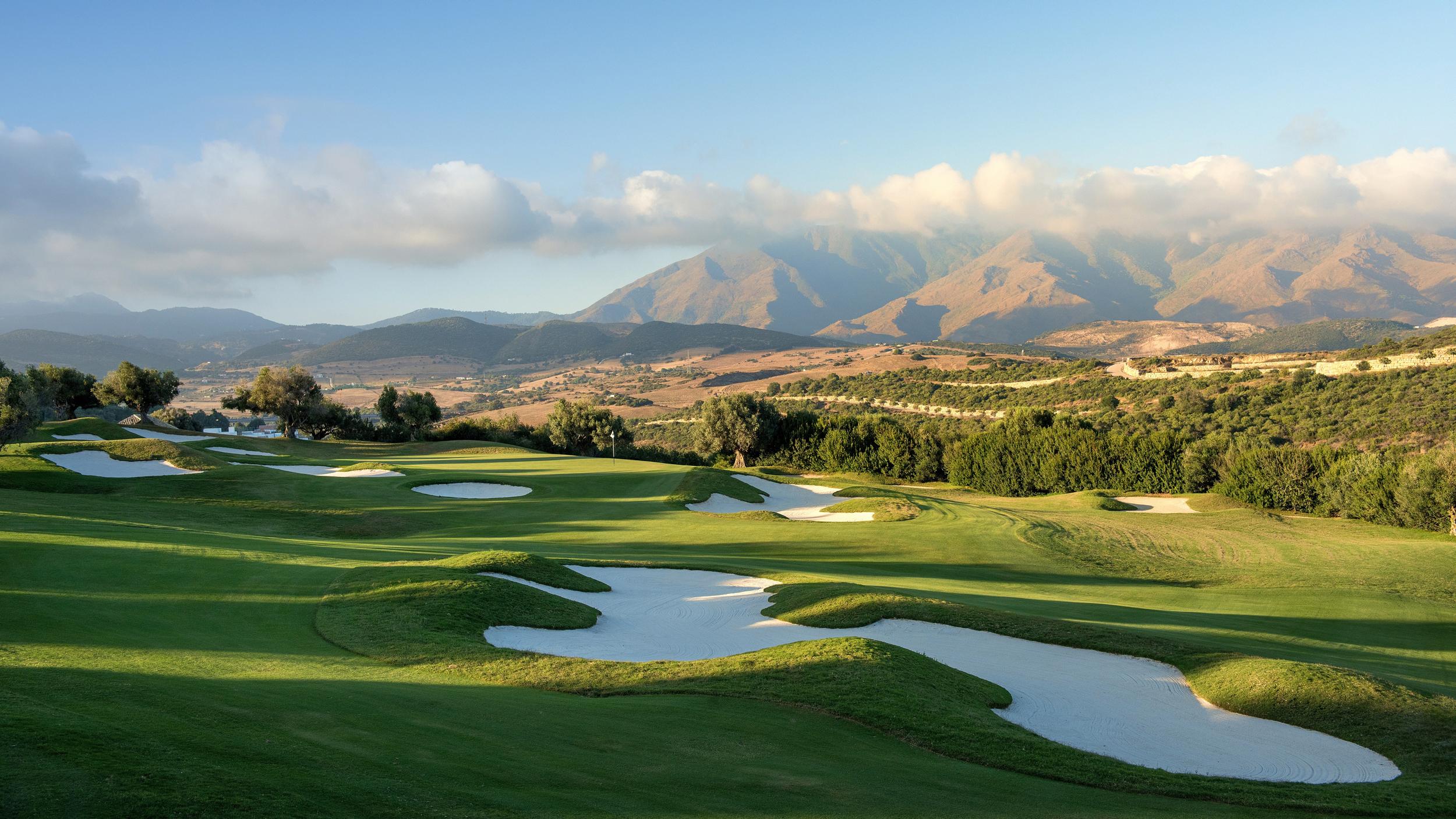 A well maintained fairway nestled with sand bunkers and mountain views in the distance