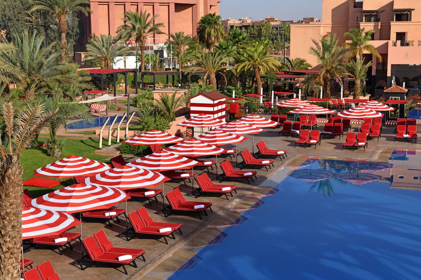 Overhead view of the outdoor swimming pool at Movenpick Mansour Eddahbi Hotel surrounded by red sunbeds