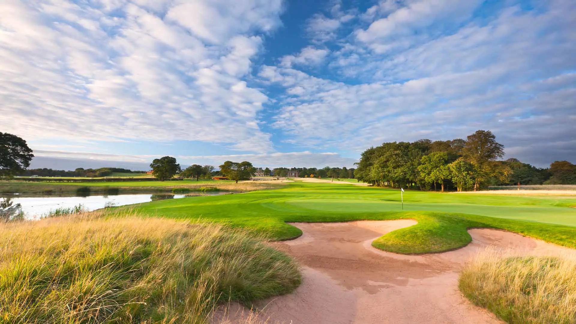 A well maintained fairway next to a water hazard nestled with sand bunkers
