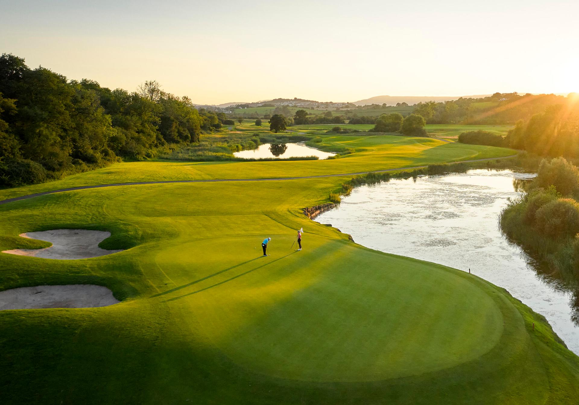 Overhead view of the sun shining onto a well maintained fairway next to a water hazard