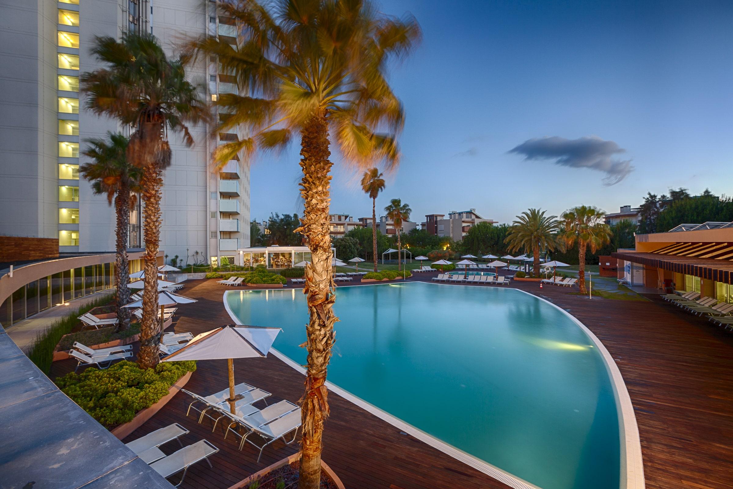 Outdoor swimming pool surrounded by sunbeds and palm trees at Troia Resort - Aqualuz Suite Hotel Apartments