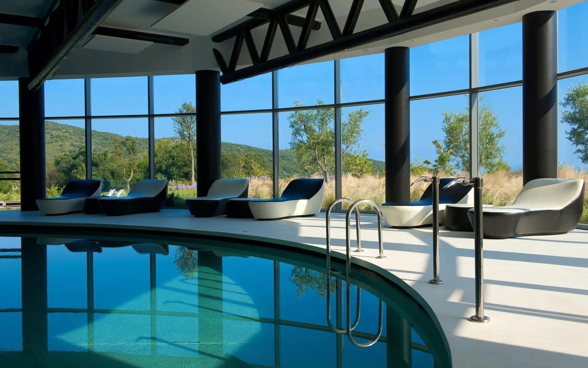 Indoor pool with panoramic window views at Argentario Resort Golf and Spa