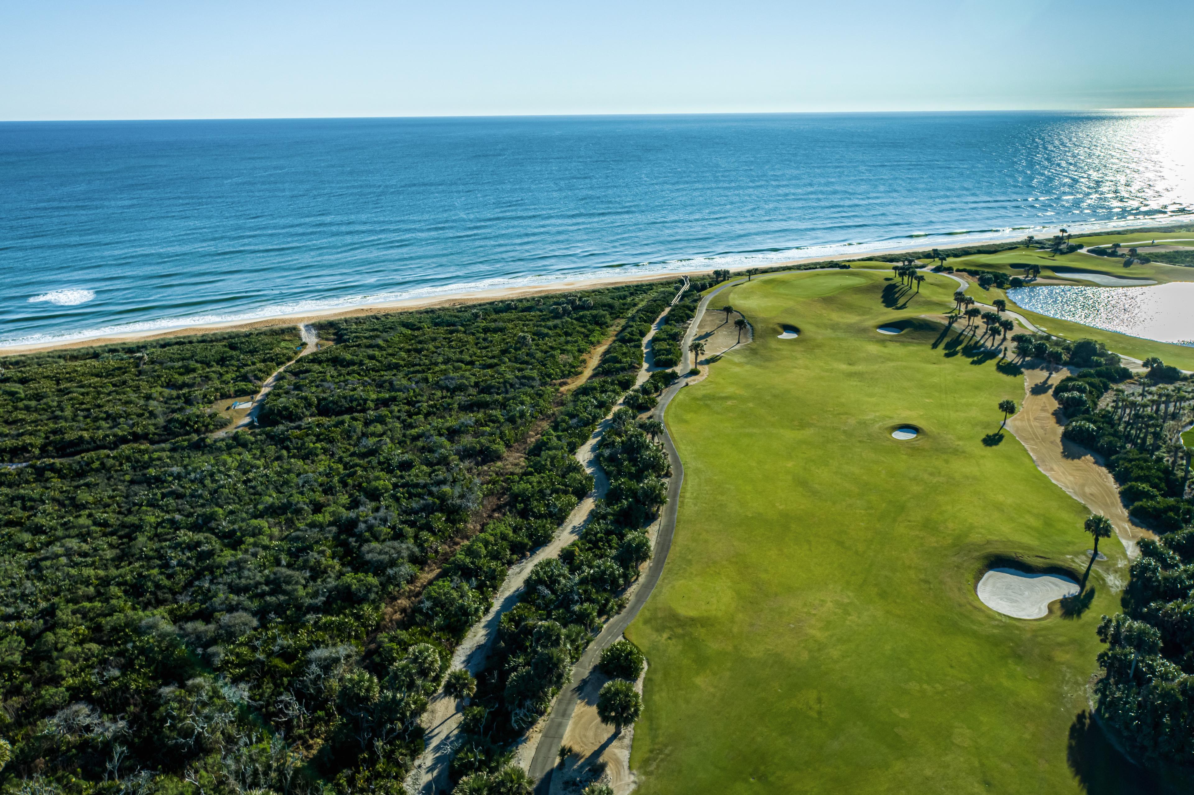 A well maintained fairway nestled with sand bunkers leading to the coast
