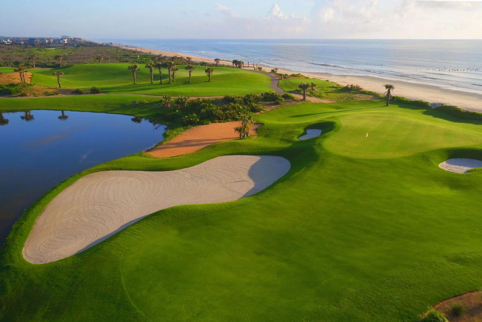 A smooth coastal green sandwiched by the coast and a large sand bunker