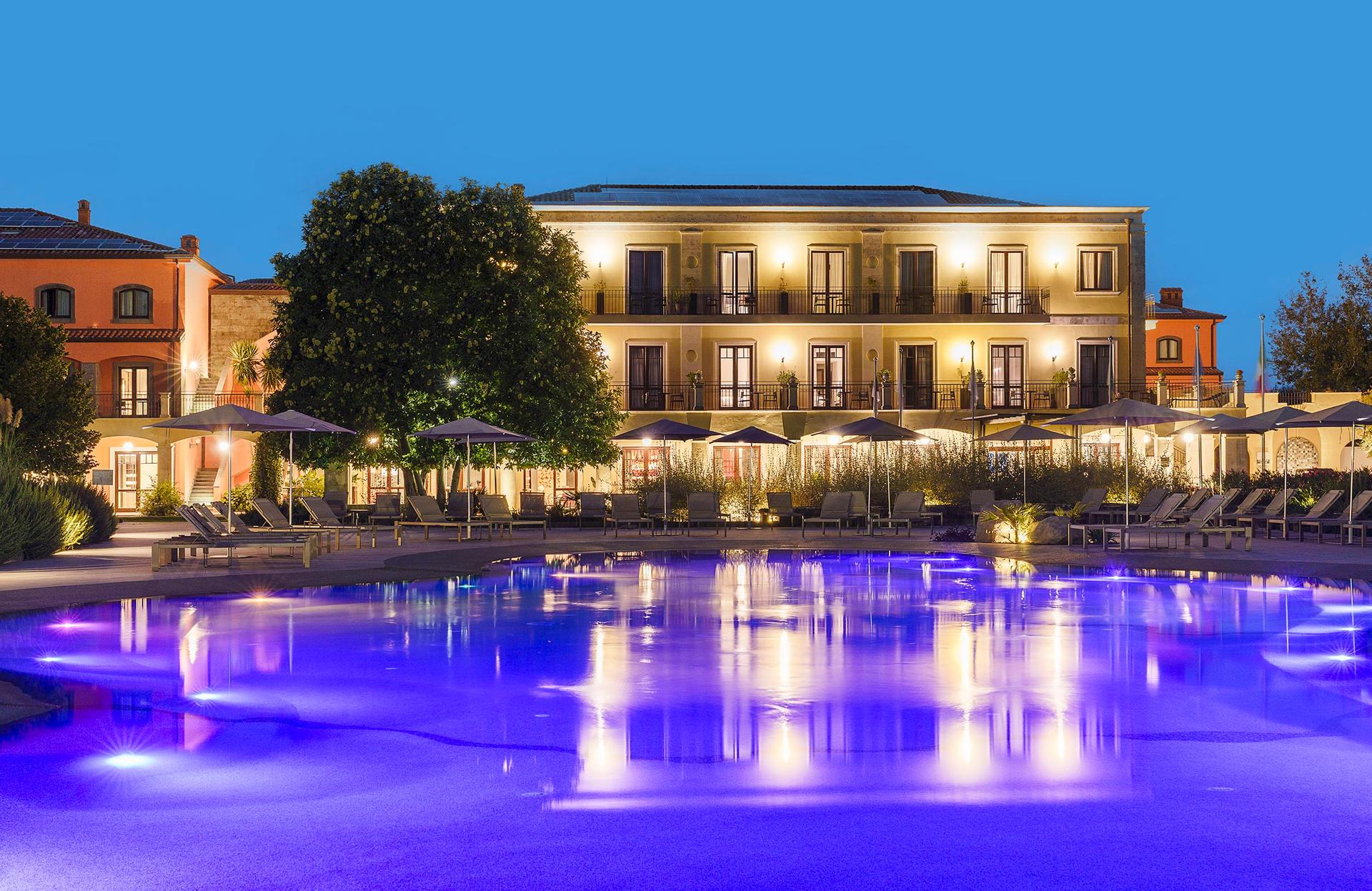 Panoramic view of the Il Picciolo Etna Golf Resort & Spa, Curio Collection by Hilton building overlooking the outdoor pool illuminated with purple light
